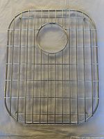 Top view of the stainless steel sink strainer grid showing the rectangular grid with central circular drain opening.