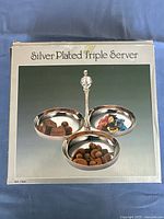 Box showing image of the silver plated triple server with the three compartment trays containing chocolates and candy, illustrating the product