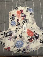 White floral print dress with thin straps, mixed red, blue, and purple flowers on white base visible with lot tag 53 attached.