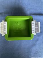 Top view of green plastic container part of tofu press, featuring Tofuture logo and white clamp on each side for pressure adjustment.