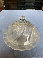 Clear vintage glass candy dish with lid showing the swirl textured pattern and scalloped edges.