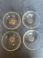 Overhead view of 4 clear glass bowls showing scalloped rims and embossed fruit designs on the bottom interior surface.