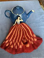 Front view of teapot with ceramic dancer and knitted cozy showing colors and design details