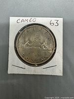Front side view of the 1963 Canadian Silver Dollar coin with 'Voyageur' design in a cardboard coin holder with writing CAMEO 63 on it.
