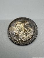 Close up of one side of the Mexican 25 Peso silver coin showing the national emblem with eagle, snake, and cactus and inscribed 'Estados Unidos Mexicanos 25 PESOS 720 LEY'. The surface shows tarnish and weathering.