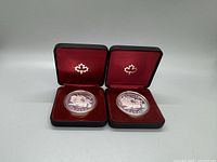 Two 1981 Canadian silver dollar proof coins in black leather presentation cases with red velvet interior and silver maple leaf stamp.