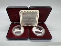 Two 1986 silver proof coins in plastic capsules placed inside red velvet-lined black leather case, leaf embossed interior with certificate card between coins.
