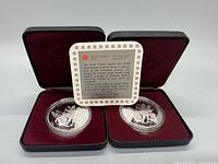 Two silver proof coins in black RCM leather cases with red velvet interiors, along with a certificate of authenticity card.