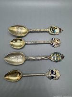 Four sterling silver souvenir spoons laid flat showing front side with enamel crests and detailed handles