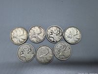 Seven Canadian silver quarters arranged with reverse side showing caribou and denomination.