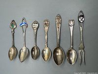 Full view of seven sterling silver souvenir spoons and fork, showing enamel crests and overall condition