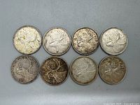 Eight Canadian silver quarters arranged in two rows, obverse side showing caribou design, with wear and tarnish visible.