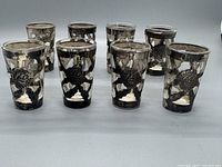 Set of 8 vintage Mexican sterling silver overlay shot glasses with floral and leaf designs.