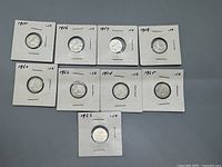 Nine Canadian 10 cent silver coins individually housed in white cardboard holders with dates written on the corners.