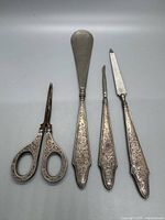 Photo showing entire manicure set laid flat including scissors, shoehorn, nail pick, and nail file with detailed engravings on handles.