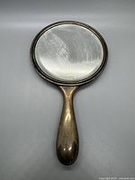 Front side of the oval Art Nouveau style hand mirror showing the reflective surface and handle shape.