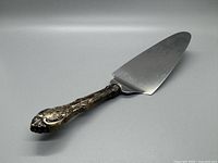 Side angle showing ornate sterling silver handle and flat serving blade with wear