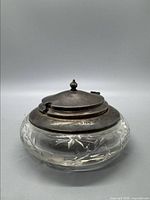 Front view of the sugar dish showing the etched floral glass bowl and tarnished sterling silver hinged lid with finial on top, with broken hinge visible.