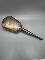 Hairbrush front side showing the Art Deco patterned silver back and tapered handle.