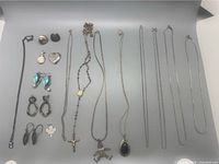 Overview of the lot showing 14 pieces of vintage sterling silver jewelry including chains, pendants, and earrings.
