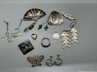 Lot of multiple vintage sterling silver jewelry pieces arranged on a flat surface, showing diverse shapes and styles including earrings, pins, brooch, and pendants with visible patina and wear.