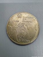 Reverse side showing Olympic rings, world map, text "Montreal 1976 Olympiade XXI Olympiad" and denomination "5 Dollars." Some wear visible.