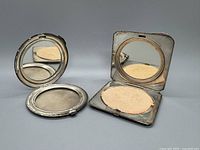 Front and inside view of both compacts showing the mirror and fabric-lined powder compartments.