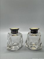 Front view of pair of clear Czech-Bohemian glass salt and pepper shakers with thick multi-faceted bases and domed blackened sterling silver lids.