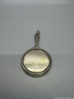 Front view of a small vintage sterling silver vanity mirror pendant showing reflective circular surface and handle with attachment ring.