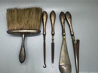 Top-down view of all five grooming pieces showing brush and four tools with ornate engraved silver handles and natural bristles on brush.