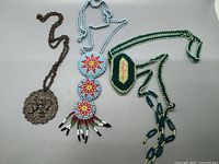 Front view of three vintage Native jewelry necklaces: metal pendant necklace with turquoise-colored stones, blue beaded necklace with red and white flower beadwork, green beaded necklace with hexagonal pendant.