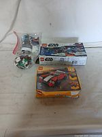 Photo showing both Lego kits on a white surface: an opened Star Wars Lego set with pieces in bags and a worn unopened Lego Creator sport car kit box.