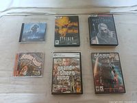 Six PC game boxes and discs: The Thing, S.T.A.L.K.E.R., The Witcher, RollerCoaster Tycoon, Grand Theft Auto IV, Mass Effect 3, arranged on a flat surface for lot overview.