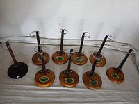 Nine doll stands arranged in rows on a white cloth backdrop, showing wood bases with green stickers and one black base.
