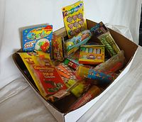 Wide view of assorted vintage drugstore toys in original packaging inside cardboard box on white cloth background