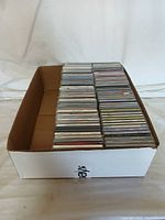 Box holding an assortment of various music CDs stacked in rows within a white cardboard box.