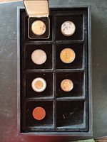 Seven coins displayed in black velvet tray with eight compartments