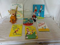 Five Dr. Seuss books arranged behind a soft plush figure and a set of Dr. Seuss blocks, displayed on a white surface.