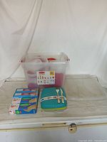Clear plastic food storage containers with red lids in a large box, turquoise meal container with fork and spoon attached, and four boxes of bags including storage and sandwich bags.