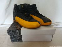 Side view of the pair of Nike Jordan basketball shoes showing black and yellow colorway on and beside a white and black shoebox