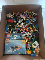 Top down photo of box filled with multicolored loose Lego bricks and three visible instruction booklets on top.