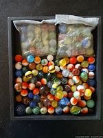Photo of two resealable bags filled with assorted cats eye marbles and loose multicolored glass marbles spread at the bottom of a black container