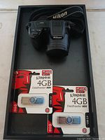 Top view of Nikon camera and two packaged Kingston 4GB USB flash drives in a box