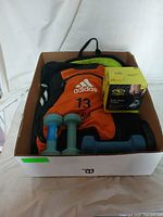 Photo showing the outdoor exercise lot in a cardboard box, including Adidas backpack, dumbbells, and boxed ankle weights.