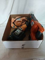 Overhead photo of 3 electric power tools packed in a cardboard box, showing a drill, belt sander, and reciprocating saw.