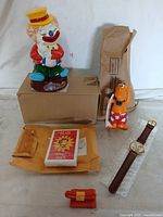 Photo showing five vintage toys including clown figurine, dog character, whistle, wristwatch, and playing cards with some items boxed.