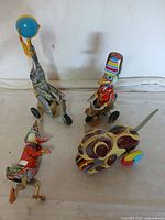 Four vintage reproduction tin toys grouped on plain background showing different animals and tricycles