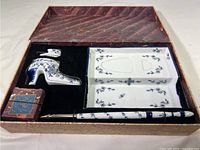 Top-down view of entire inkwell set in original box showing shoe inkwell, dip pen, ink blotter, and box.