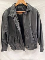Front view of the black leather jacket showing collar, buttons, and elasticized sides