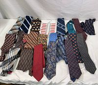Photo showing the full collection of 20 colorful men's ties laid out flat in rows with various patterns and colors including stripes, paisley, and geometric designs.